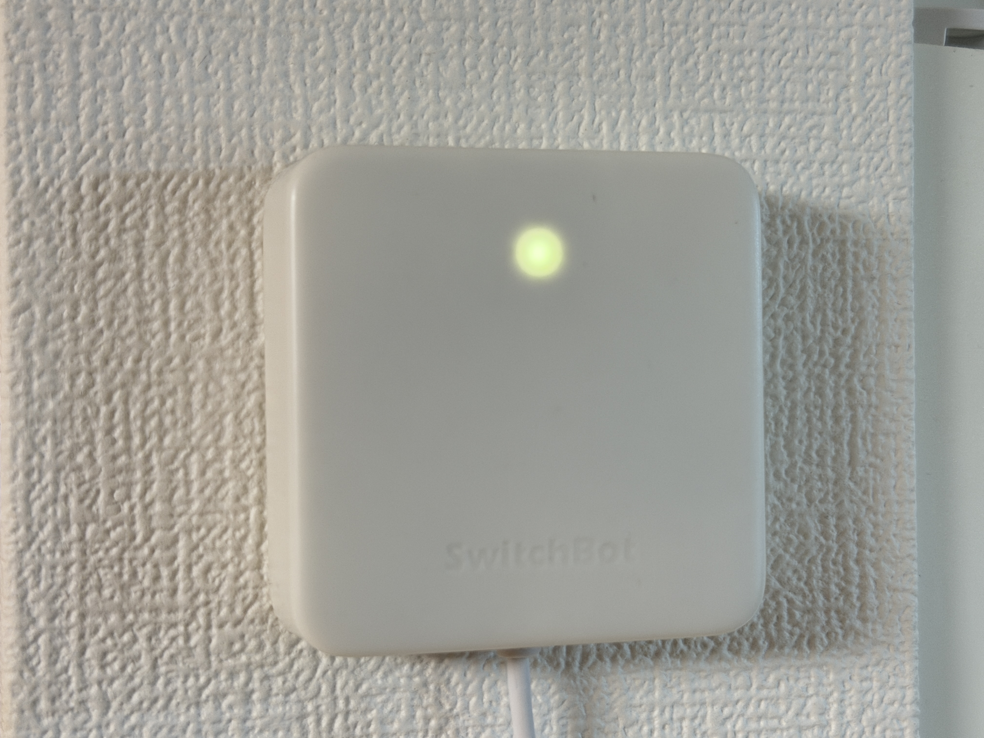 壁面に設置され緑色のランプが点灯しているSwitchBotハブミニ