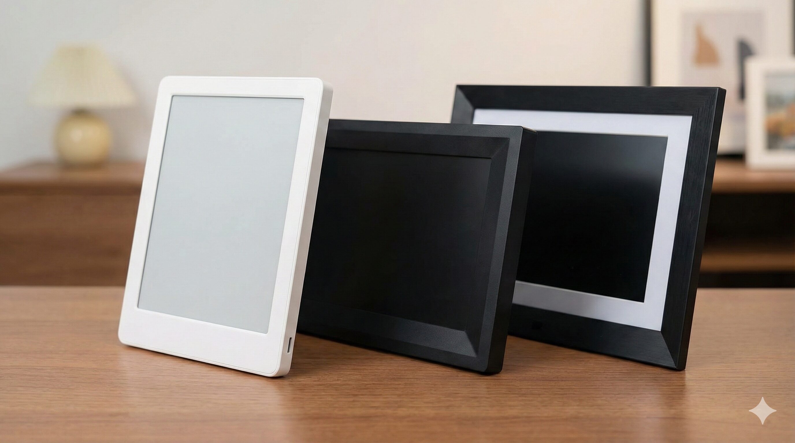 デスク上に並べられた、白い電子ペーパーアートキャンバスと、デザインの異なる他社製の黒いデジタルフォトフレーム2台の外観比較。